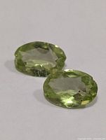 Two oval faceted peridot gemstones on white background