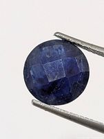 Front view of round blue sapphire held by tweezers