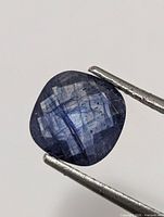 Close-up of loose blue sapphire clamped in tweezers
