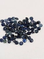 Pile of small round blue faceted sapphires on white background