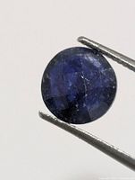 Close-up of sapphire held by tweezers showing faceted surface and colour