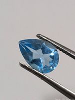 Close-up of pear-cut blue topaz held by gem tweezers