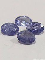Four loose oval violet-blue tanzanite gemstones on white background
