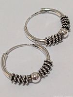 Two silver hoop earrings showing coiled wire accents and bead