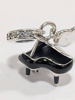 Pendant close-up showing piano shape, black enamel, and stone-set bail