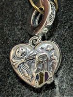 Front view showing embossed skeleton figures and enamel accents on heart pendant