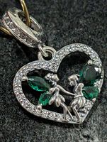 Front view of heart pendant showing fairy figures, green stones, and pavé CZ
