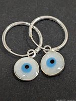 Front view of both silver hoop earrings with mother-of-pearl evil eye charms
