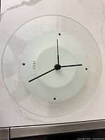 Front view of Umbra glass wall clock showing design and hands