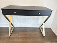 Front view of black wood desk showing two drawers and gold metal X-legs