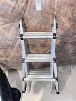 Front view of folded aluminum articulating ladder showing four sections and hinges