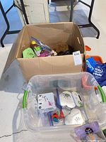 Cardboard box and clear tote with assorted toys, flash cards, plush, Kidsafe harness, LeapFrog device visible