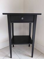 Front view of black side table showing drawer and shelf