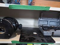 Bosch router base, black mounting plate, open Dremel case with tool and bits on shelf