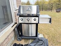 Closed Broil King stainless steel gas grill with side shelf, propane tank base and cover visible