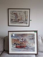 Both framed lithograph prints on wall and sofa for scale