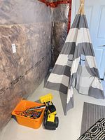 Teepee, dump truck and orange bucket of toys positioned together in the room