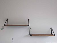 Two wooden wall shelves mounted on white wall with black metal brackets