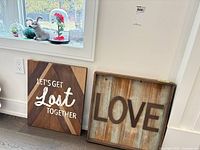 Two wood wall signs leaning against wall beside window with pressed glass items on sill