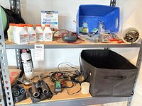 Overview of two shelves showing multimeter, oil bottles, NeverWet kit, binoculars, charger, bins, hardware