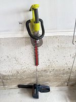 Hedge trimmer hanging on wall above chainsaw on floor