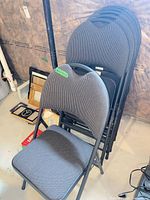 Stack of six gray/black fabric folding chairs against wall