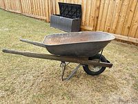 Side view of wheelbarrow showing steel tub, wood handles, pneumatic wheel, metal frame