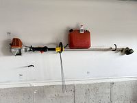 Entire trimmer mounted on wall with fuel can, oil bottle, extra line visible