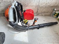 Stihl BR 600 blower, earmuffs, and red fuel can laid out on floor