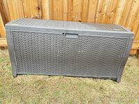 Front view of closed brown resin Suncast deck box against fence