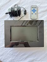 Front view of Dynex digital photo frame with remote control and power adapter
