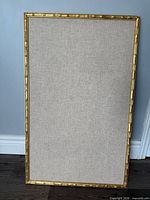 Front view of fabric-covered cork board with gold frame