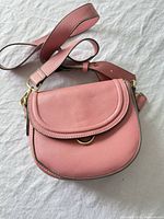 Front view of pink crossbody purse showing flap, strap and gold-tone hardware