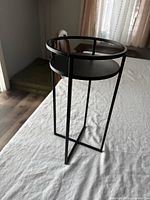 Overall view of black metal plant stand on table, showing circular top and leg structure