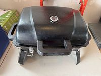 Closed view showing black portable grill with lid thermometer and folding legs