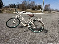 Full side view of white and teal Clairmont cruiser bicycle showing step-through frame, rear rack, teal rims