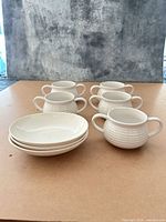 Eight stoneware pieces—five handled bowls, three shallow bowls—arranged on tabletop