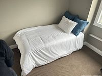 Twin bed with white duvet, white pillow, two blue decorative pillows