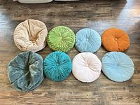Eight round velvet poufs arranged on floor showing colors and styles