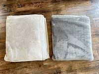 Gray and beige/taupe folded fleece blankets laid side by side on floor