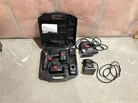 All items laid out: cordless drill with battery, charger, carry case, corded jigsaw, corded orbital sander with cords