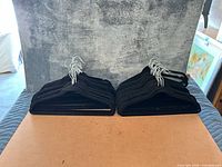 Two stacks of black velvet hangers with metal hooks