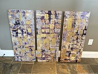 Front view showing three abstract canvases with gold, purple, silver tones
