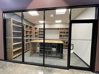 Office view showing multiple wooden shelving units with island and glass wall