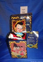 Front view of open jack-in-the-box showing Pinocchio figure, artwork on front panel, original box behind, certificate visible
