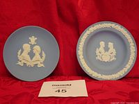 Both Wedgwood blue jasperware commemorative plates side by side on red backdrop with lot number card