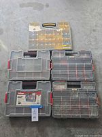 Five organizer cases arranged on floor, clear lids show compartments filled with metal fasteners