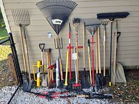 Full lineup of rakes, shovels, forks, axes and other tools leaning against wall