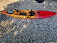 Full view of Perception Pescador 12.0 kayak with paddle and seat on gravel surface