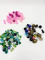 Three separate piles of beads showing pink set, green/teal mix and earth-tone mix